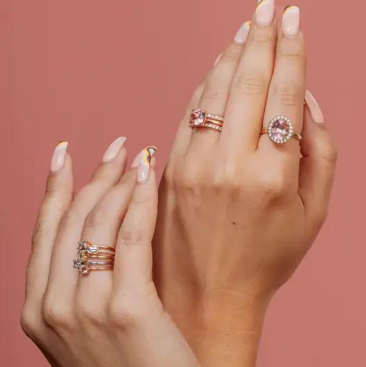 Two hands wearing rings with pink gemstones